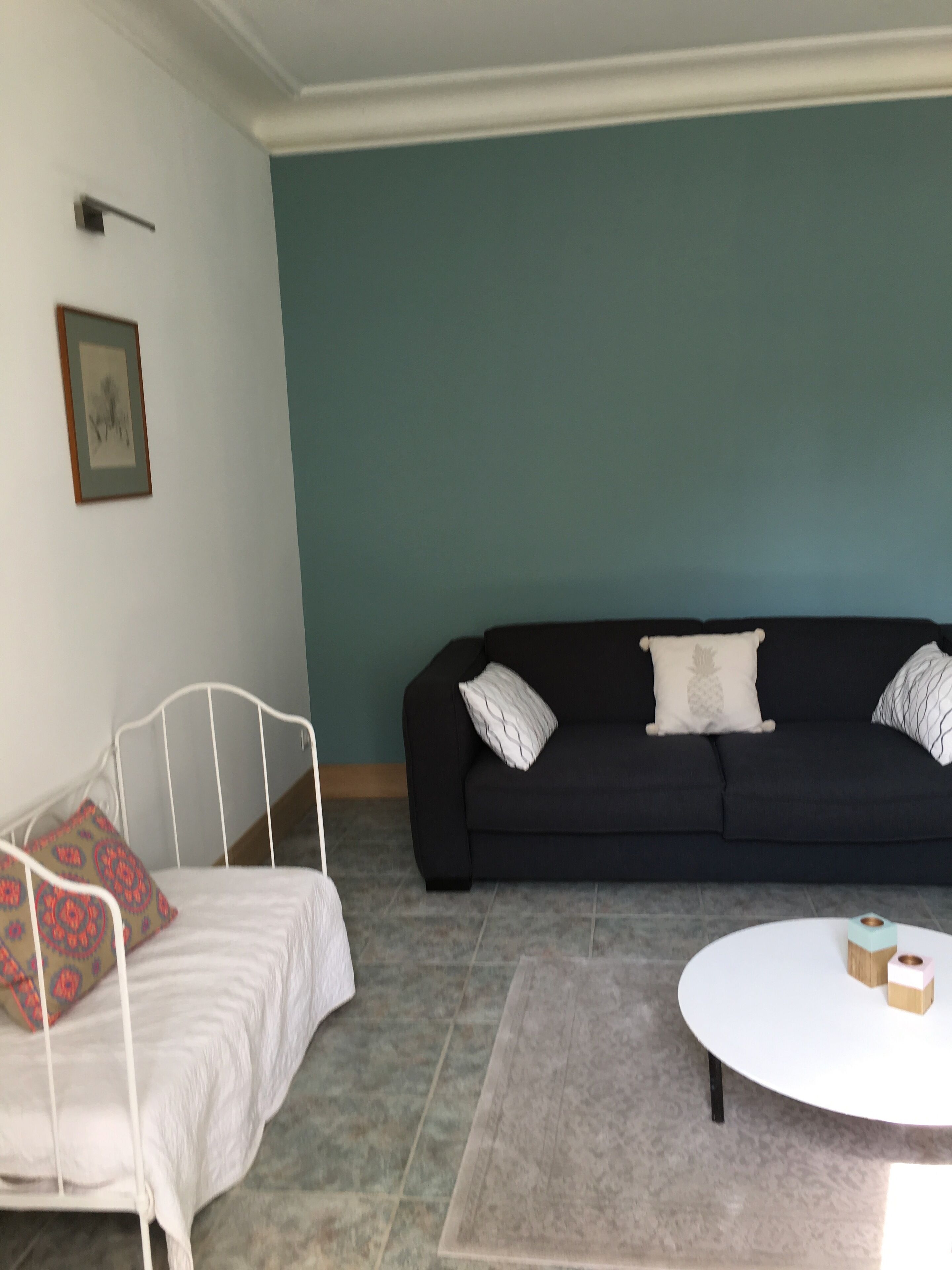 Un soggiorno con una struttura letto in metallo bianco, un divano nero con cuscini decorati e un tavolino da caffè bianco.