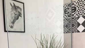 Una habitación moderna con un panel de vidrio, un cuadro enmarcado de un caballo, una planta en maceta y baldosas estampadas.