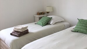 Un dormitorio con dos camas, cada una con ropa blanca y almohadas estampadas de color verde. Hay una mesita de noche con una lámpara y una caja de pañuelos.