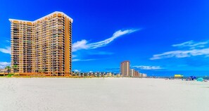 Un hotel moderno con numerosi balconi, situato vicino a una spiaggia sotto un cielo azzurro intenso.