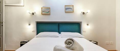 A hotel room with a large bed, a teal headboard, two wall-mounted light fixtures, and a skylight above.