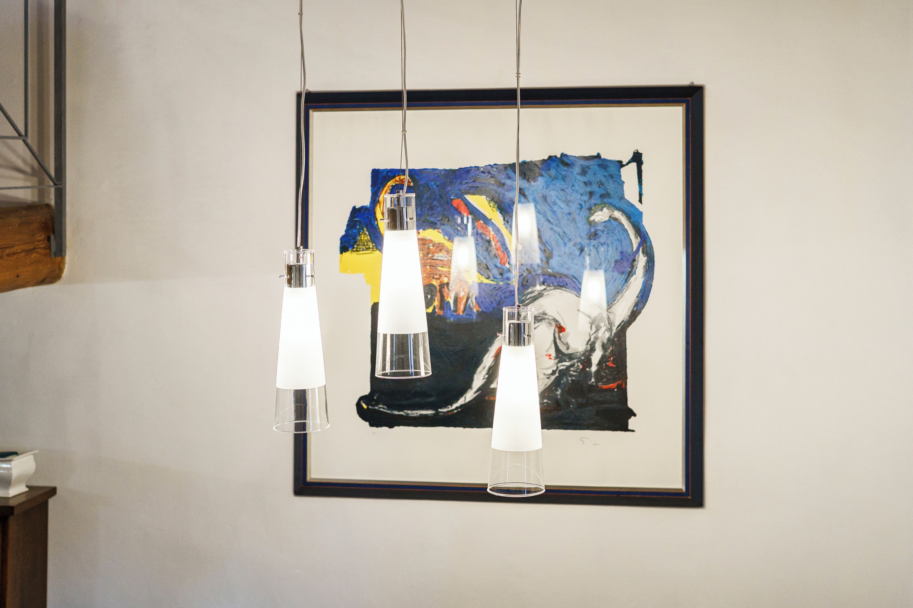 A framed abstract painting with three hanging pendant lights.