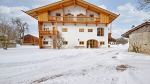 Eine zweistöckige Holzhütte mit Balkon, großen Fenstern und einer verschneiten Auffahrt.