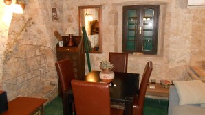 A rustic dining area with a wooden table, chairs, and a window with green shutters. - Stone house DAN (Sveti Filip i Jakov)