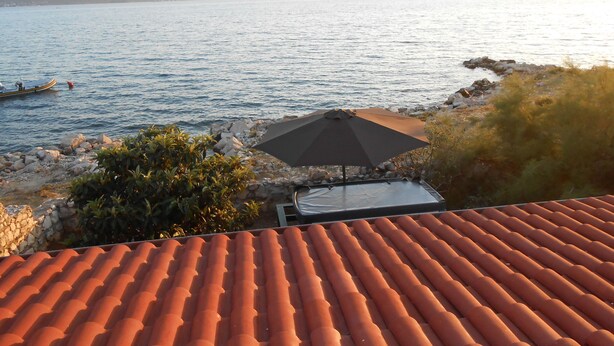 A terrace with a tiled roof overlooking a body of water, a rocky shoreline, and a distant mountain range. - Stone house DAN (Sveti Filip i Jakov)