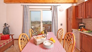 Un coin repas avec une nappe à carreaux, des chaises en bois, un panier à pain en osier et une vue à travers une porte vitrée.
