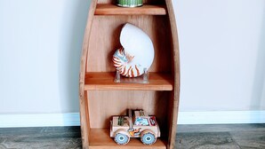 Una repisa de madera con forma de barco que tiene tres niveles, cada uno con diferentes objetos decorativos.