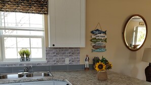 Una cocina con gabinetes blancos, encimera de granito, salpicadero de ladrillo y ventana con un adornos geométricos.