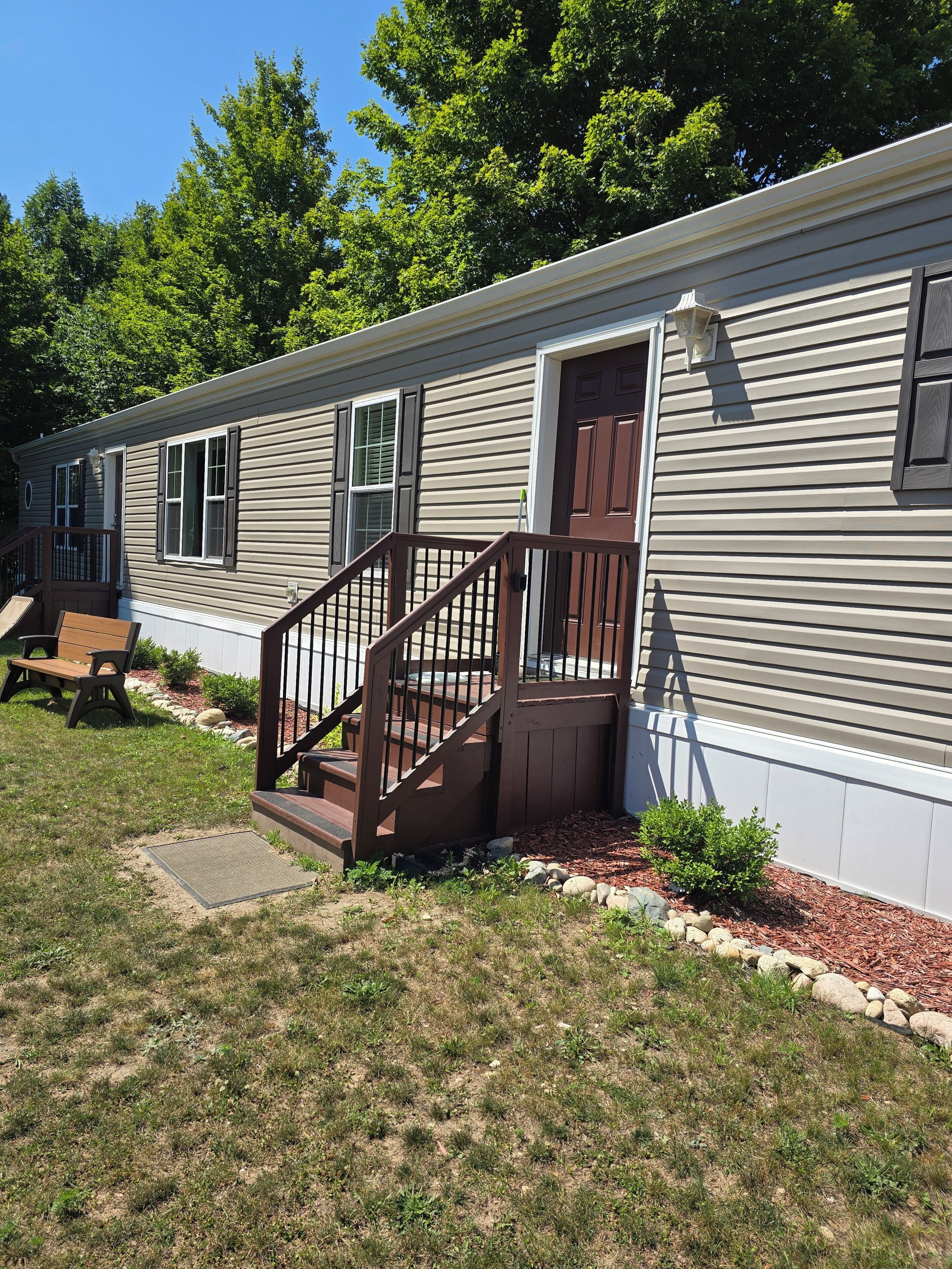 A single-story mobile home with a front porch, a wooden staircase, and a bench.