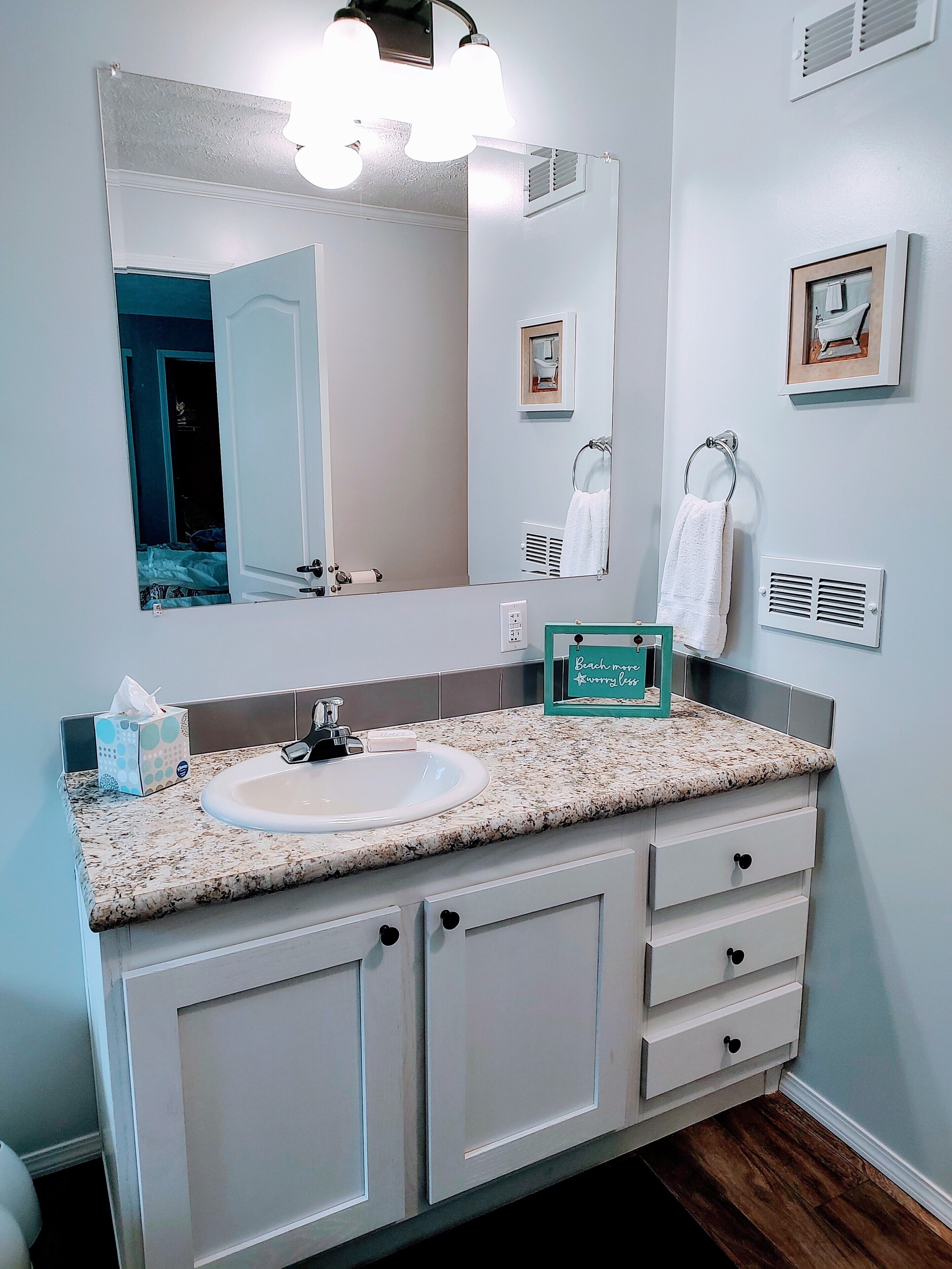 A bathroom with a white sink, a large mirror, and a vanity with drawers.