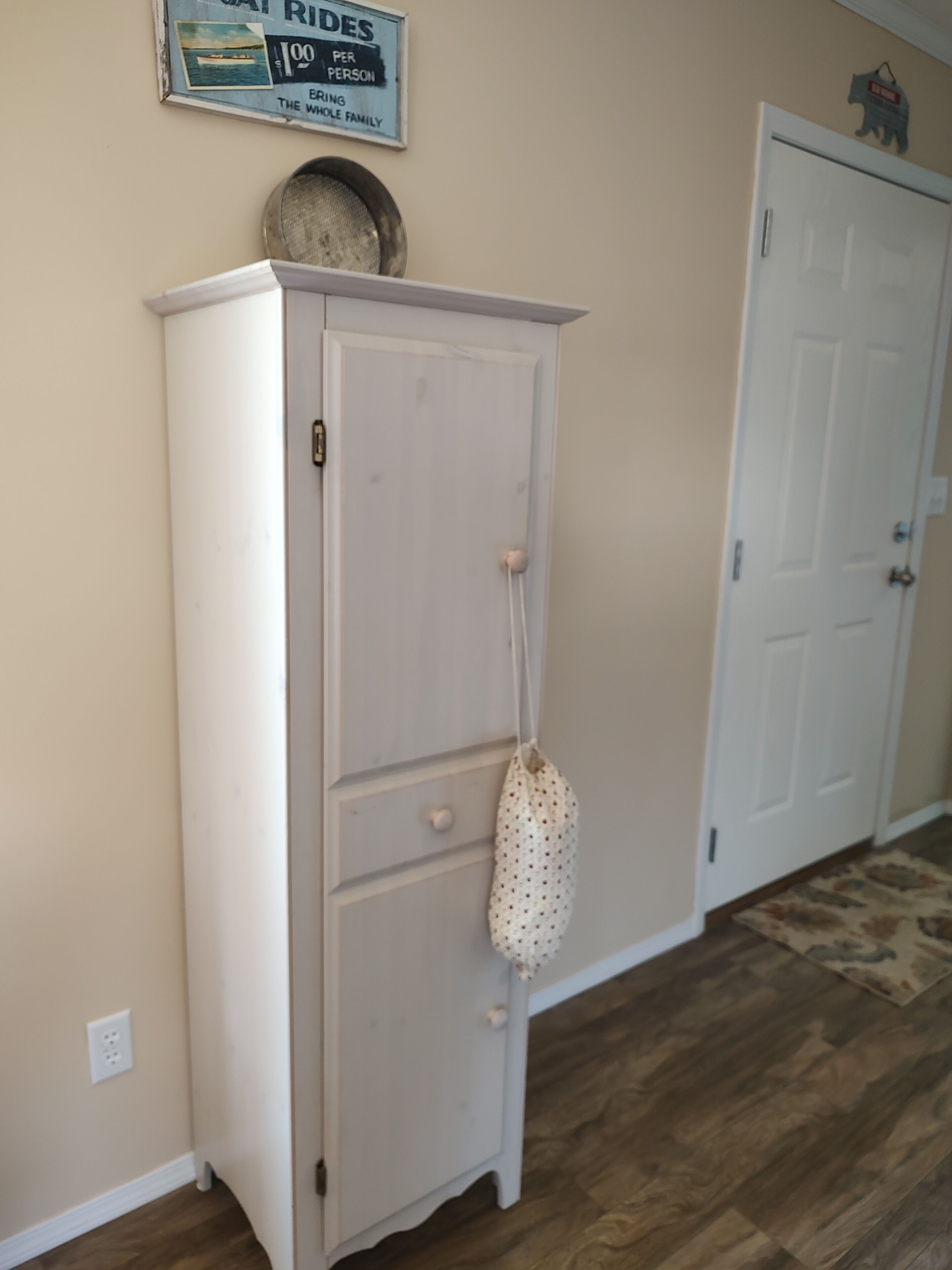 A white cabinet with a small bag hanging on it, a door, and a sign on the wall.