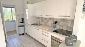 Una cocina moderna con armarios blancos, un lavamanos, una cafetera y un cubo de basura.