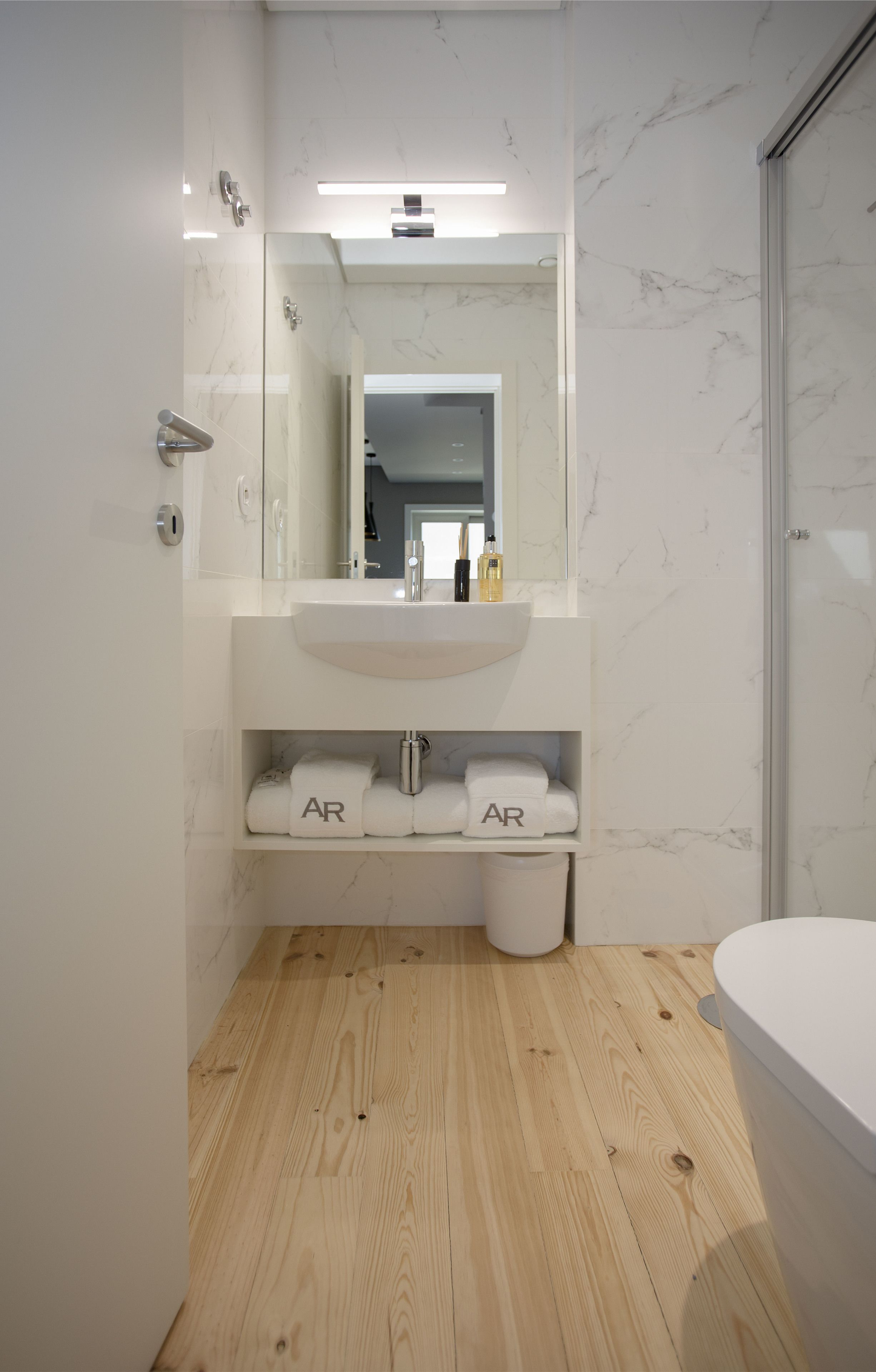 Un bagno moderno con un lavandino bianco, pareti in marmo e un pavimento in legno, oltre a un box doccia in vetro.