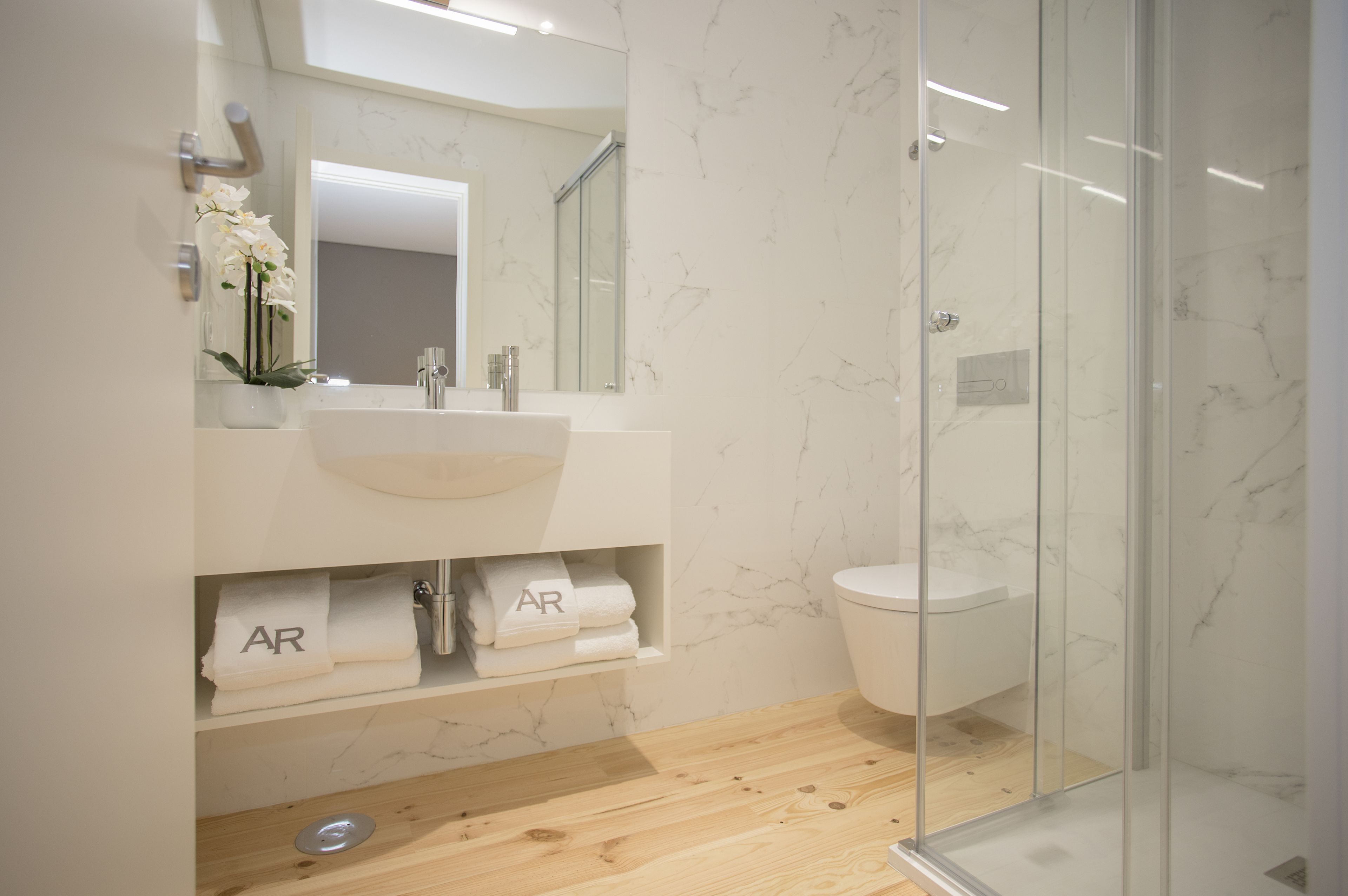 Une salle de bain moderne avec un lavabo en marbre, une douche en verre et un plancher en bois.