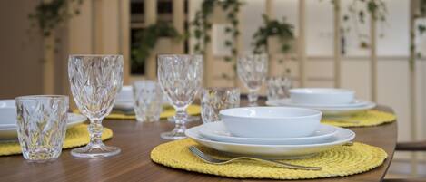A dining table set with clear glassware and white plates, with a woven placemat and a fork on it.