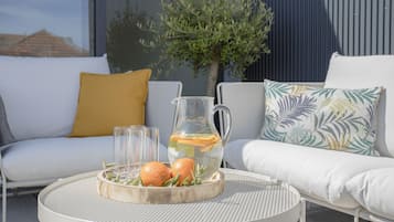 A round table with a pitcher of water, two oranges, and a tray of greenery.