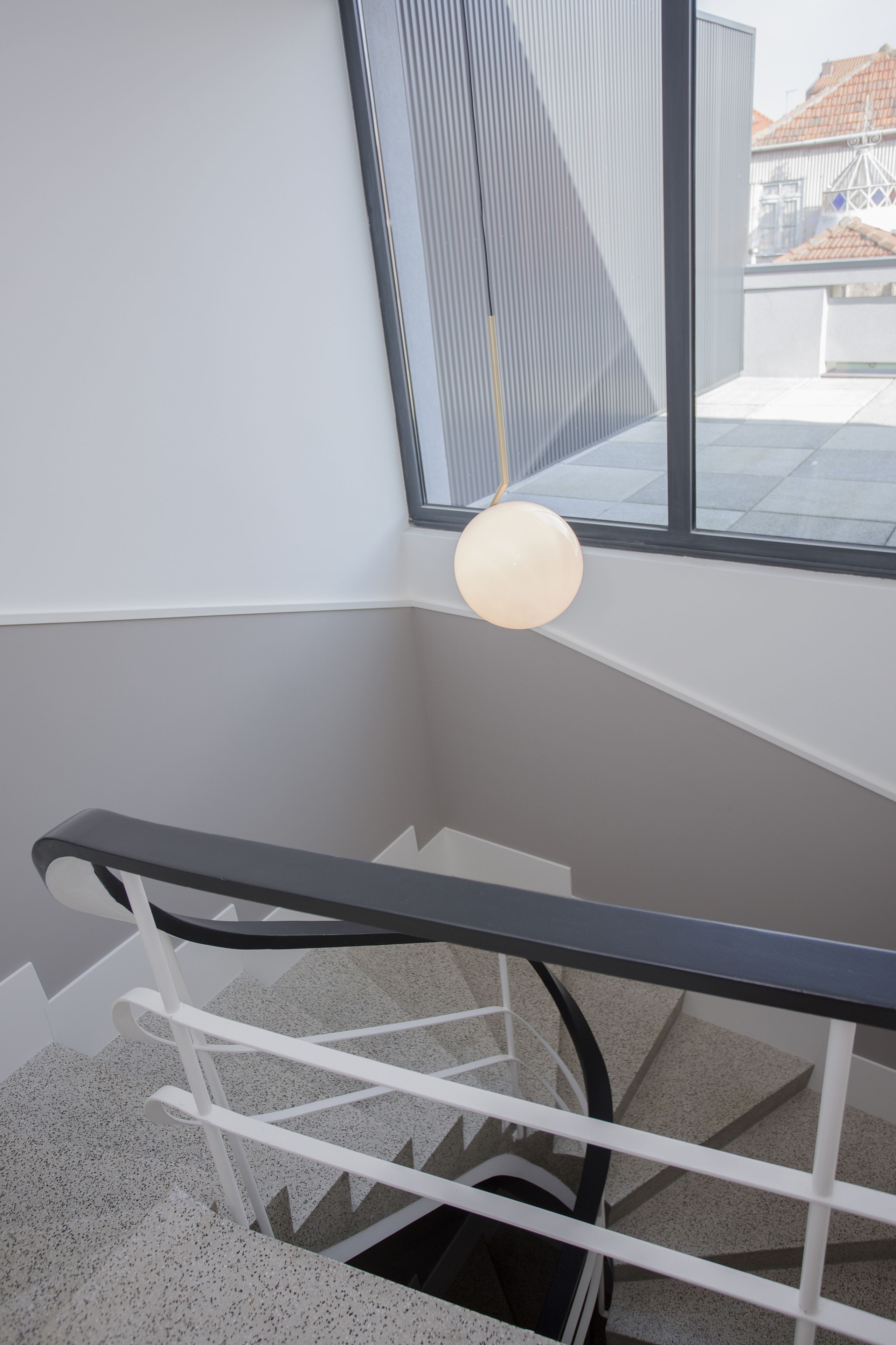 A modern staircase with a black handrail and white balusters, leading to a landing with a large window offering a view of buildings outside.