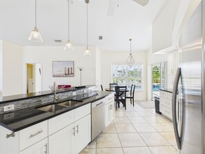 A modern kitchen with a large island, stainless steel appliances, pendant lighting, and a dining area with chairs.