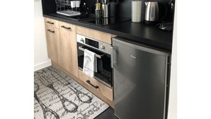 A modern kitchen with wooden cabinets, a stainless steel refrigerator, a built-in oven, and a black countertop.