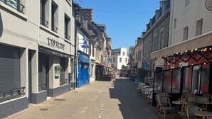 A street with buildings, a café with outdoor seating, and a clear blue sky.