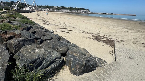 A beach with a large Ferris wheel, rocky shoreline, and buildings in the background.