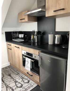 Eine moderne Küche mit Holzausbau, einem Edelstahlkühlschrank, einem eingebauten Backofen und einer schwarzen Arbeitsplatte.