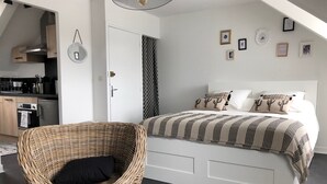 A modern bedroom with a large bed, a wicker chair, a kitchenette, and a ceiling light.