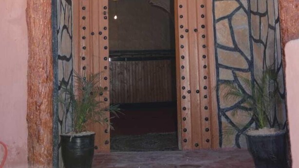 Una porta de fusta amb claus metàl·liques decoratives i el número '8' a la part superior, amb plantes en testos a banda i banda.