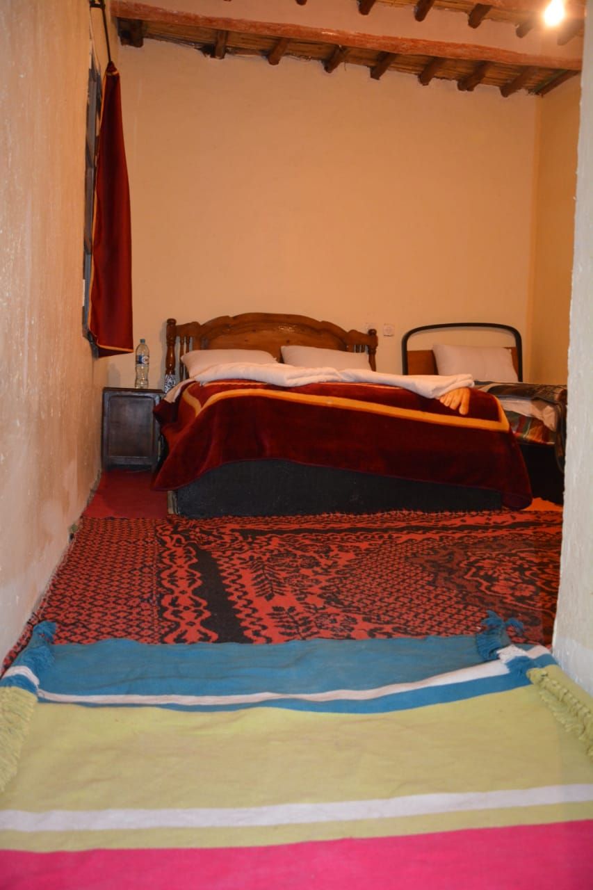 A bedroom with two beds, a wooden headboard, a nightstand, and a red and blue patterned rug.