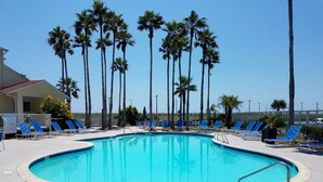 A swimming pool with blue water, surrounded by lounge chairs and palm trees. - Awesome Beach Retreat, 1st Floor, Walking Distance To  the Beach, Pool, Hot Tub (Corpus Christi)