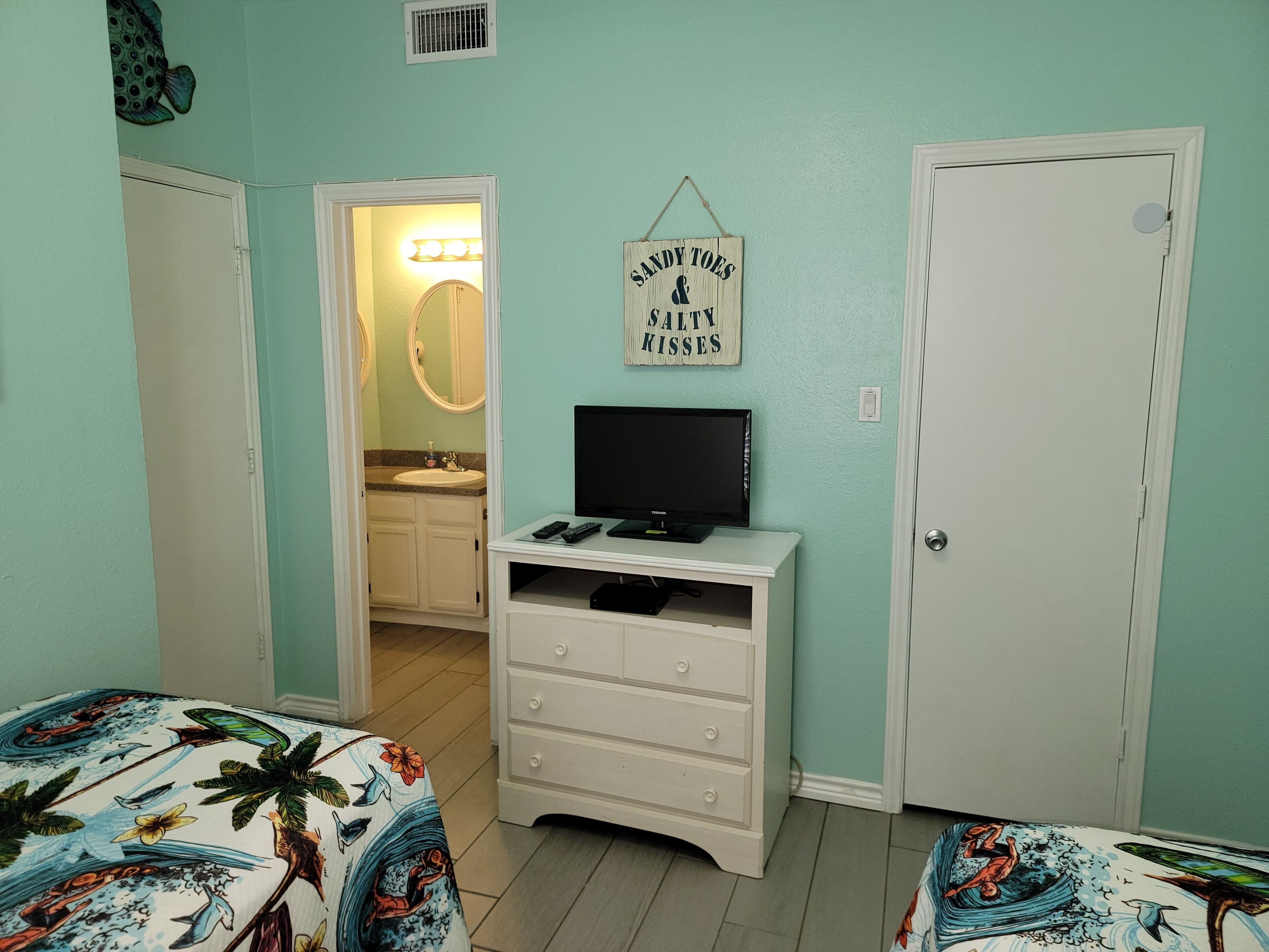 Une chambre à coucher avec un lit, une commode, un téléviseur et un panneau accroché au mur.