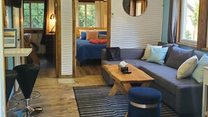 Ein gemütliches Wohnzimmer mit einer Couch, einem Couchtisch und einem Fernseher. Ein Fenster mit Vorhängen und ein Spiegel sind an der Wand angebracht.