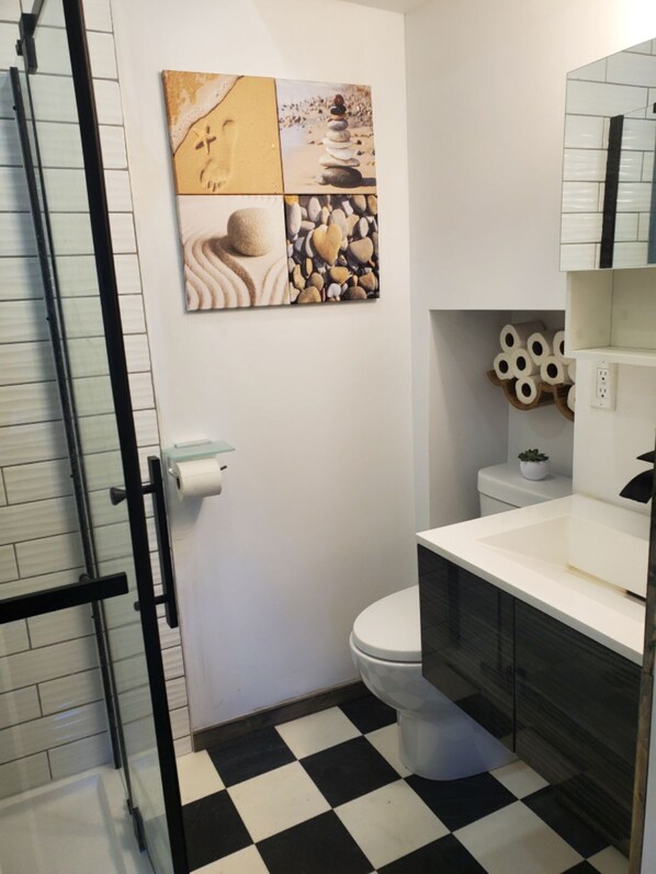 A bathroom with a black and white checkered floor, a toilet, a sink, and a shower area. - Cedar Cove Cabin Steps to Sauble Beach (Sauble Beach)