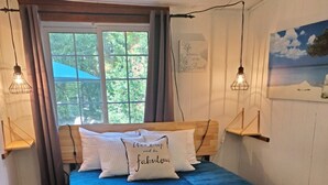 Ein Schlafzimmer mit Bett, Holz-Kopfteil und einem Fenster mit Vorhängen. An der Wand befinden sich Wandleuchten und ein Gemälde.