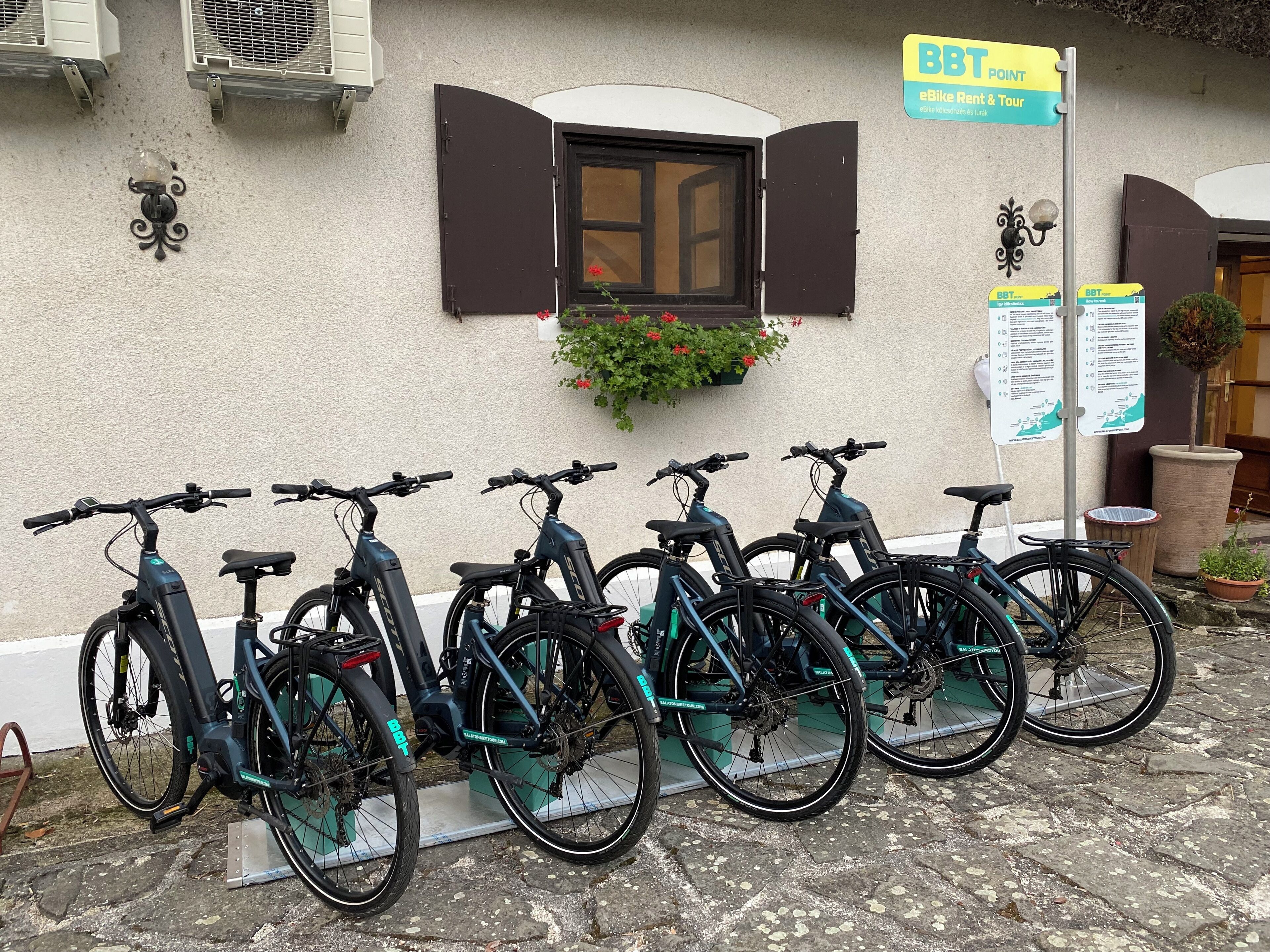 Varias bicicletas eléctricas estacionadas junto a un edificio, con un letrero que indica servicio de alquiler de bicicletas.