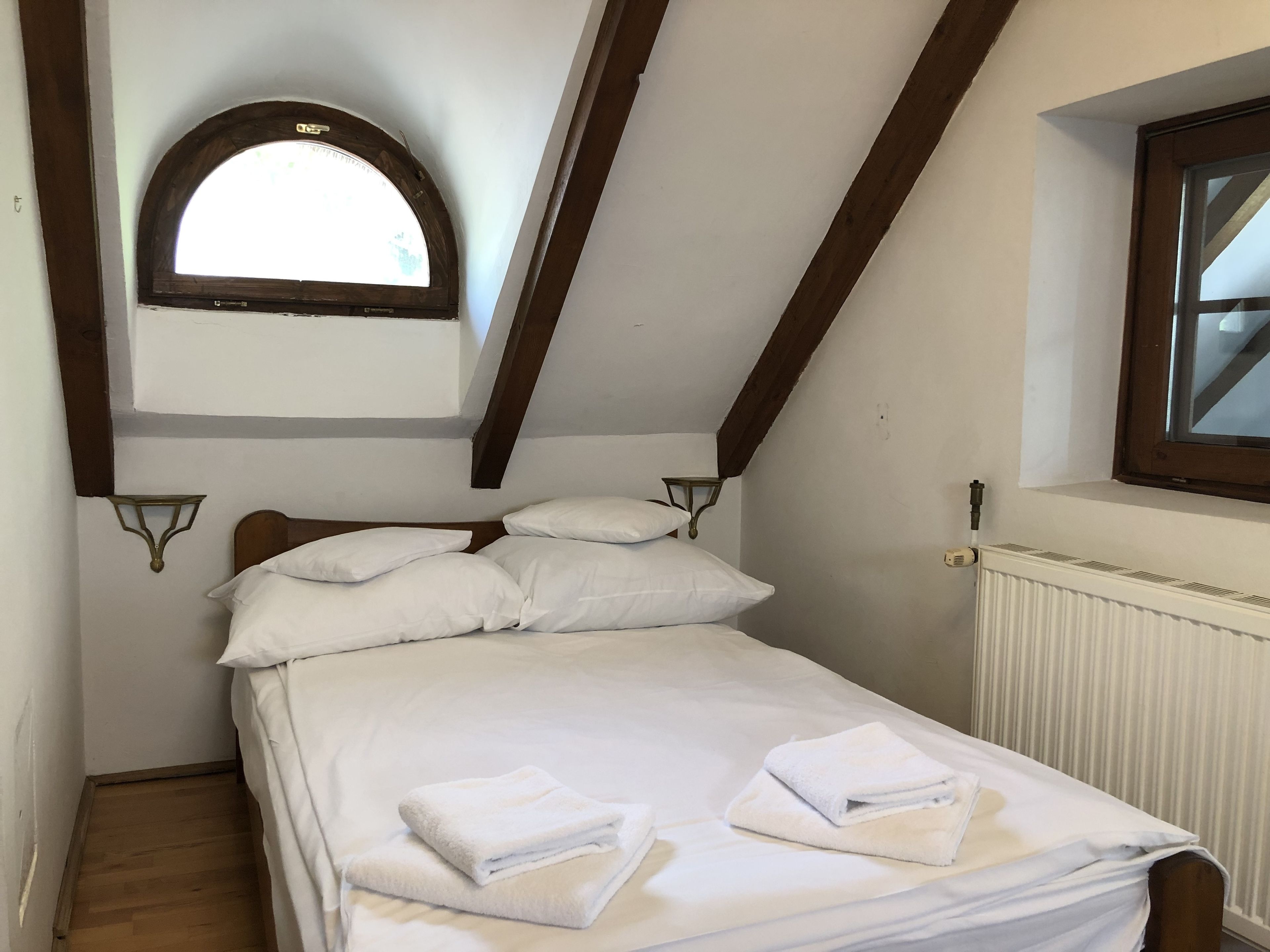 A bedroom with a sloped ceiling, a wooden headboard, white bedding, and a window with a wooden frame.