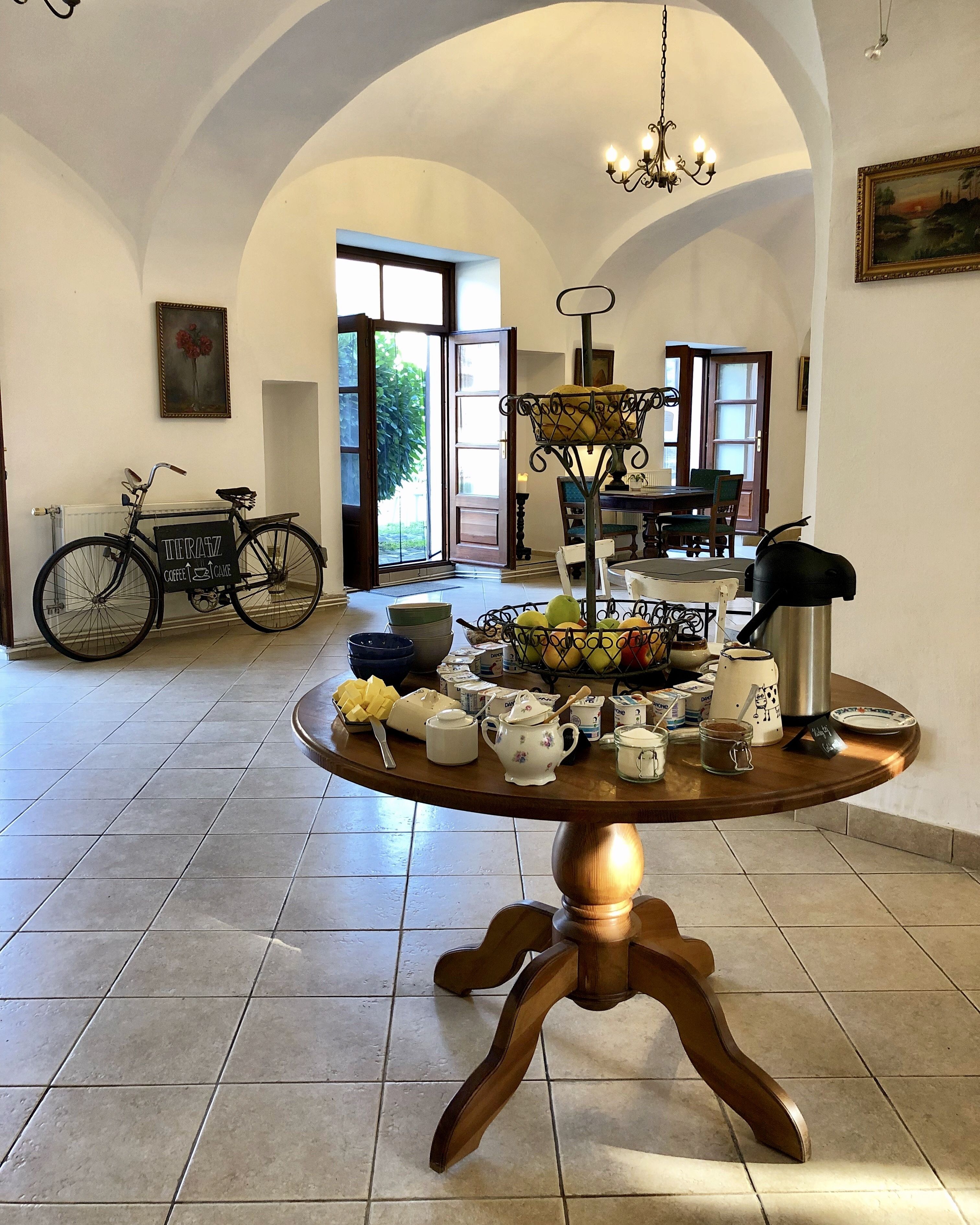 A dining area with a round wooden table set for breakfast, a bicycle, and a chandelier.