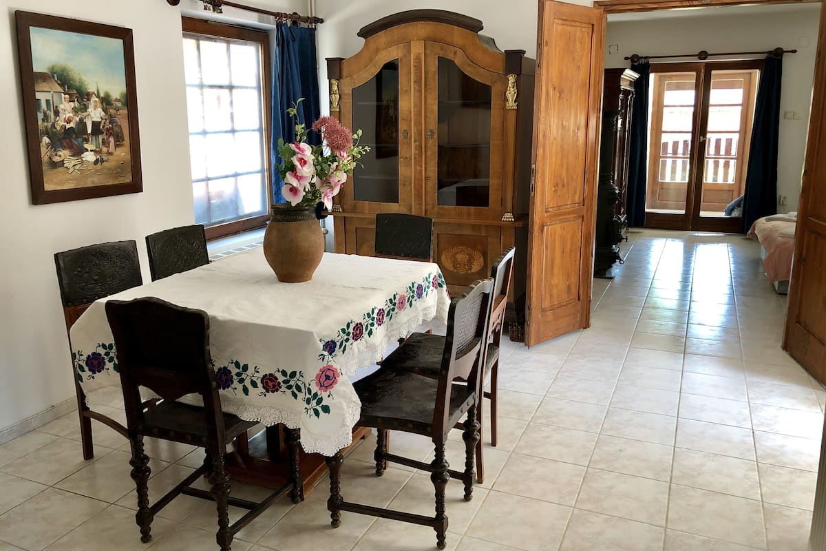 Un coin repas avec une table dressée pour quatre personnes, entourée de chaises, d’un buffet en bois et d’un vase rempli de fleurs.