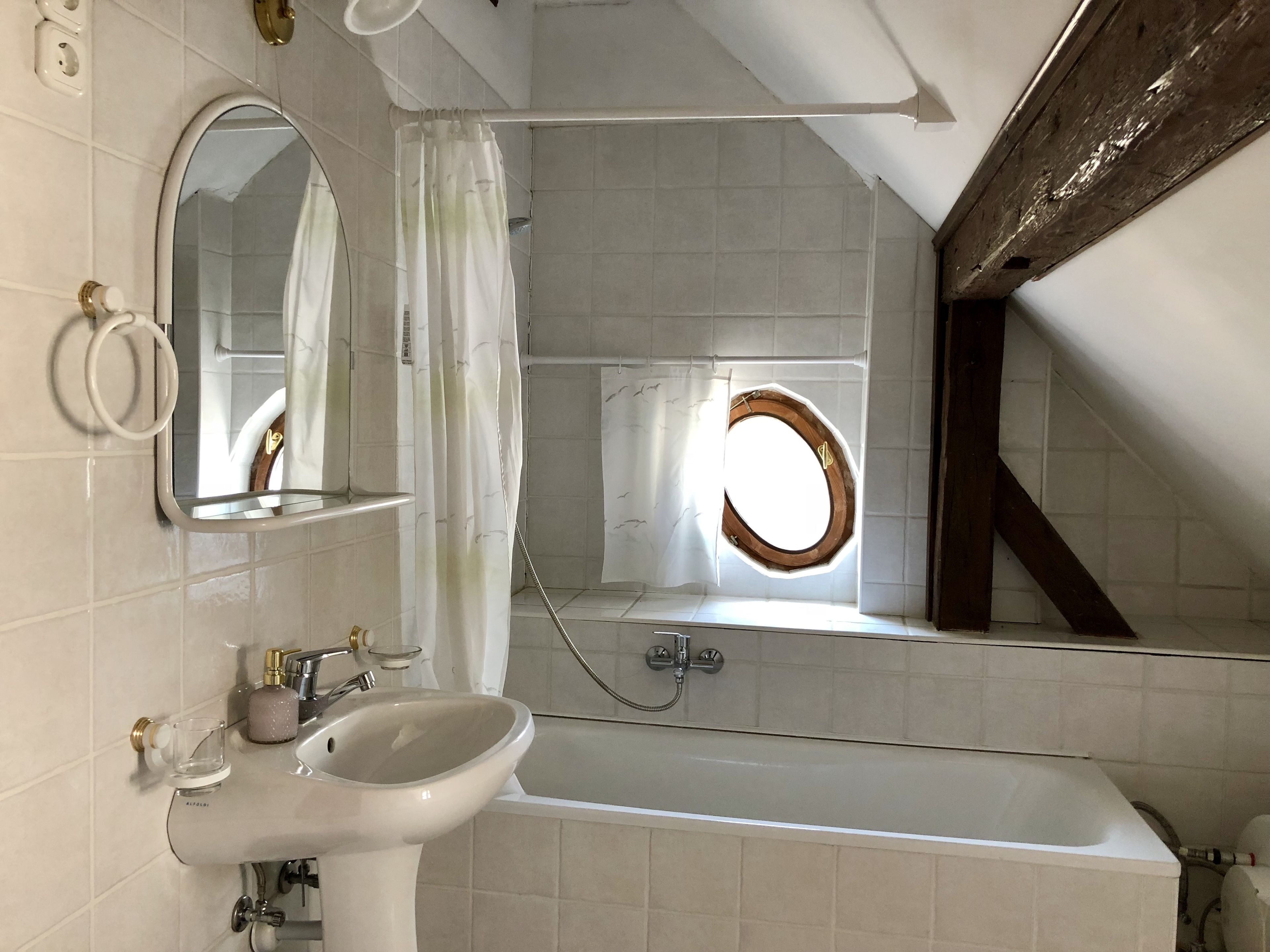 Ein Badezimmer mit Badewanne, Waschbecken, Spiegel und einem Fenster mit Holzrahmen.