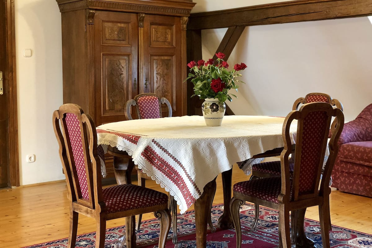 Un coin repas avec une table ronde, quatre chaises en bois, un vase de fleurs et un tapis à motifs.