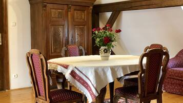 A dining area with a round table, four wooden chairs, a vase with flowers, and a patterned rug.