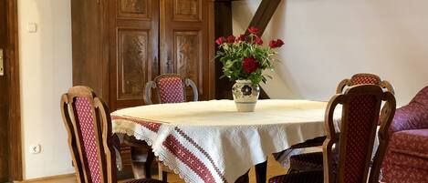 A dining area with a round table, four wooden chairs, a vase with flowers, and a patterned rug.