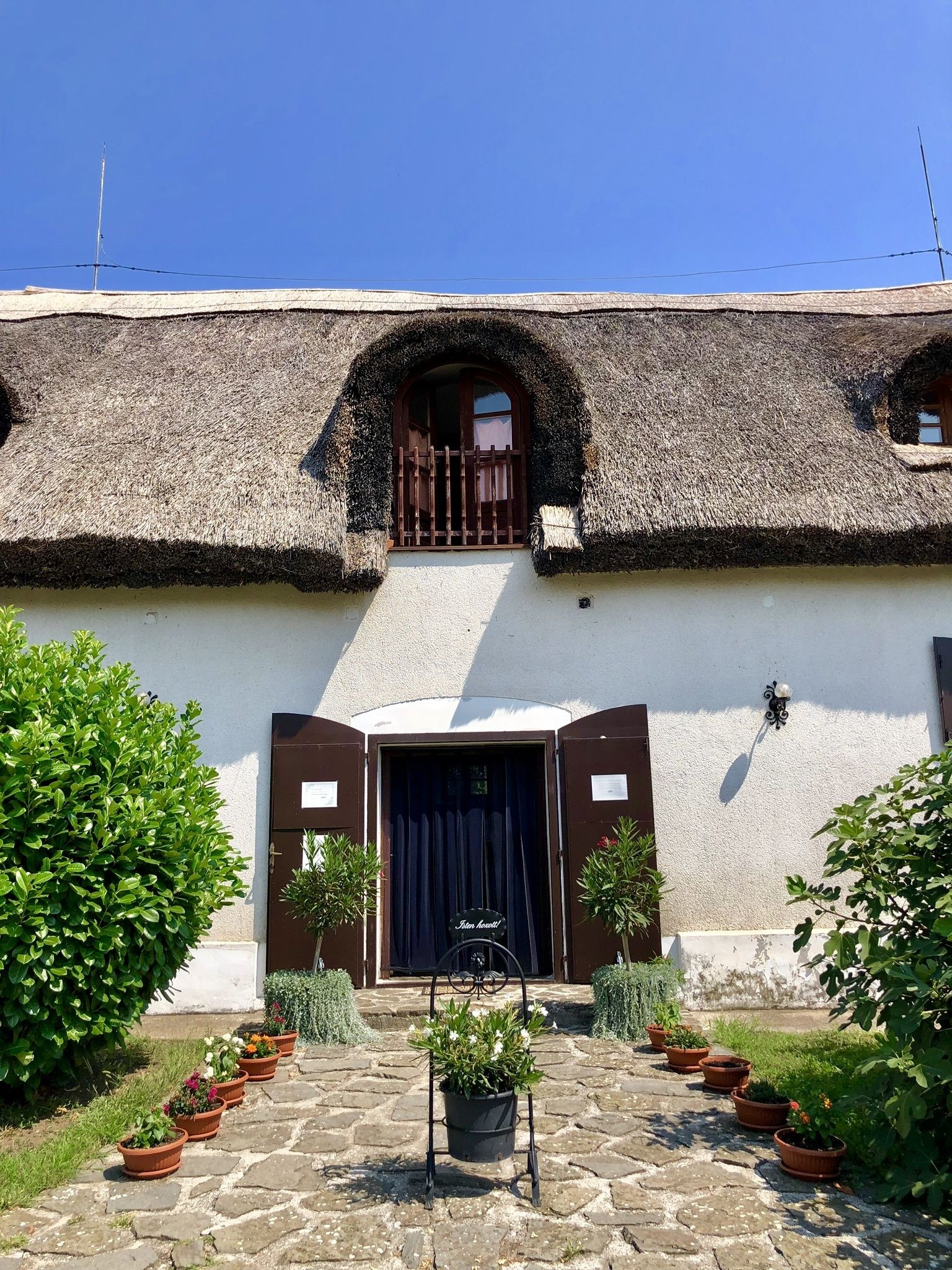 A traditional building with a thatched roof, a central entrance with a dark door, and a small balcony.