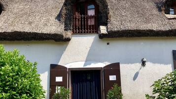 A traditional building with a thatched roof, a central entrance with a dark door, and a small balcony.