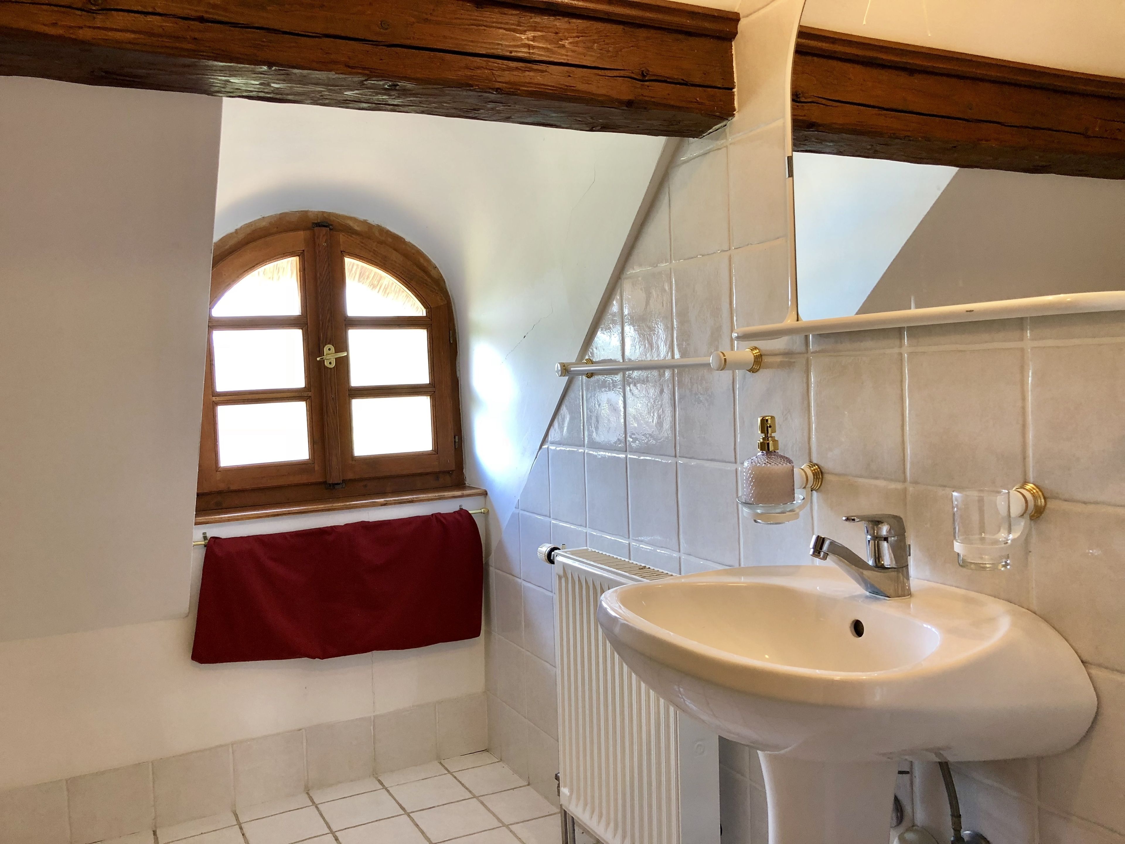 A bathroom with a white sink, a red towel, a window with wooden frames, and tiled walls.
