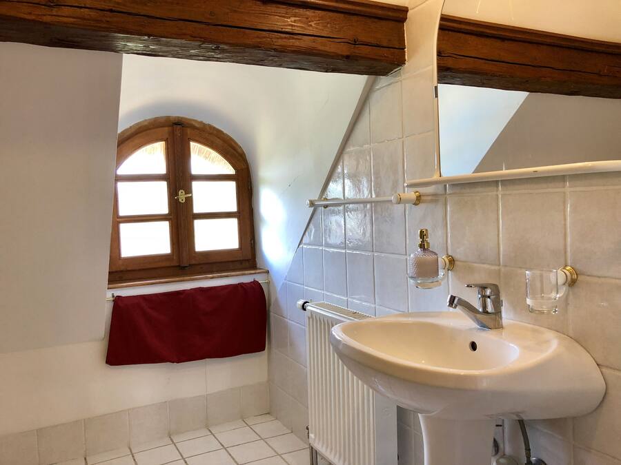 A bathroom with a white sink, a red towel, a window with wooden frames, and tiled walls.