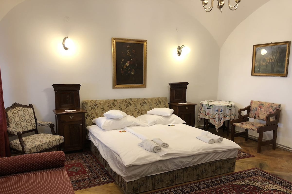 Une chambre d’hôtel avec un grand lit, deux tables de chevet, une chaise, une petite table et deux lampes fixées au mur.