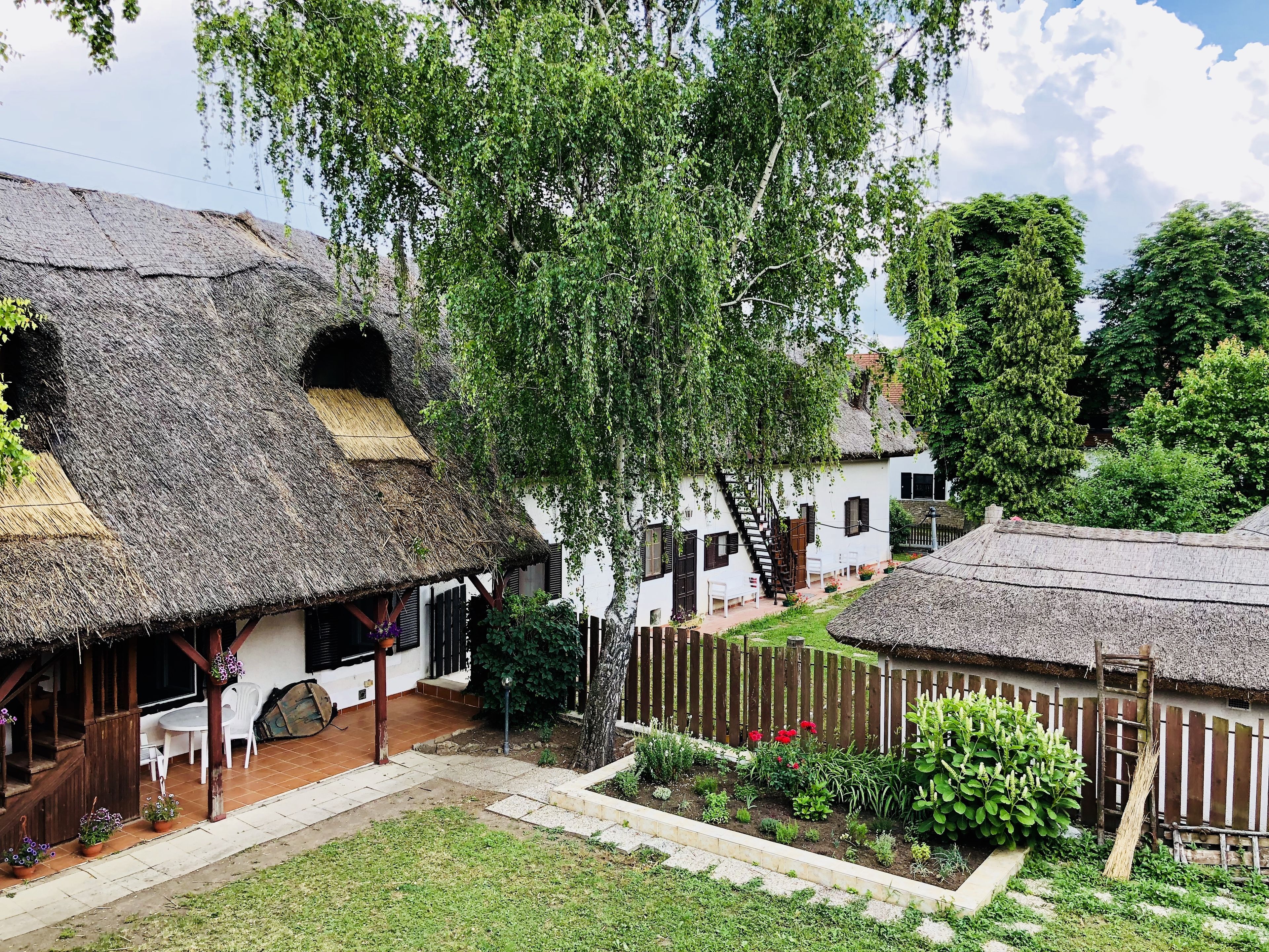 A traditional village with thatched-roof houses, a wooden fence, and a garden with various plants and flowers.