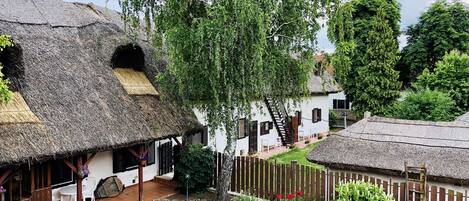 A traditional village with thatched-roof houses, a wooden fence, and a garden with various plants and flowers.