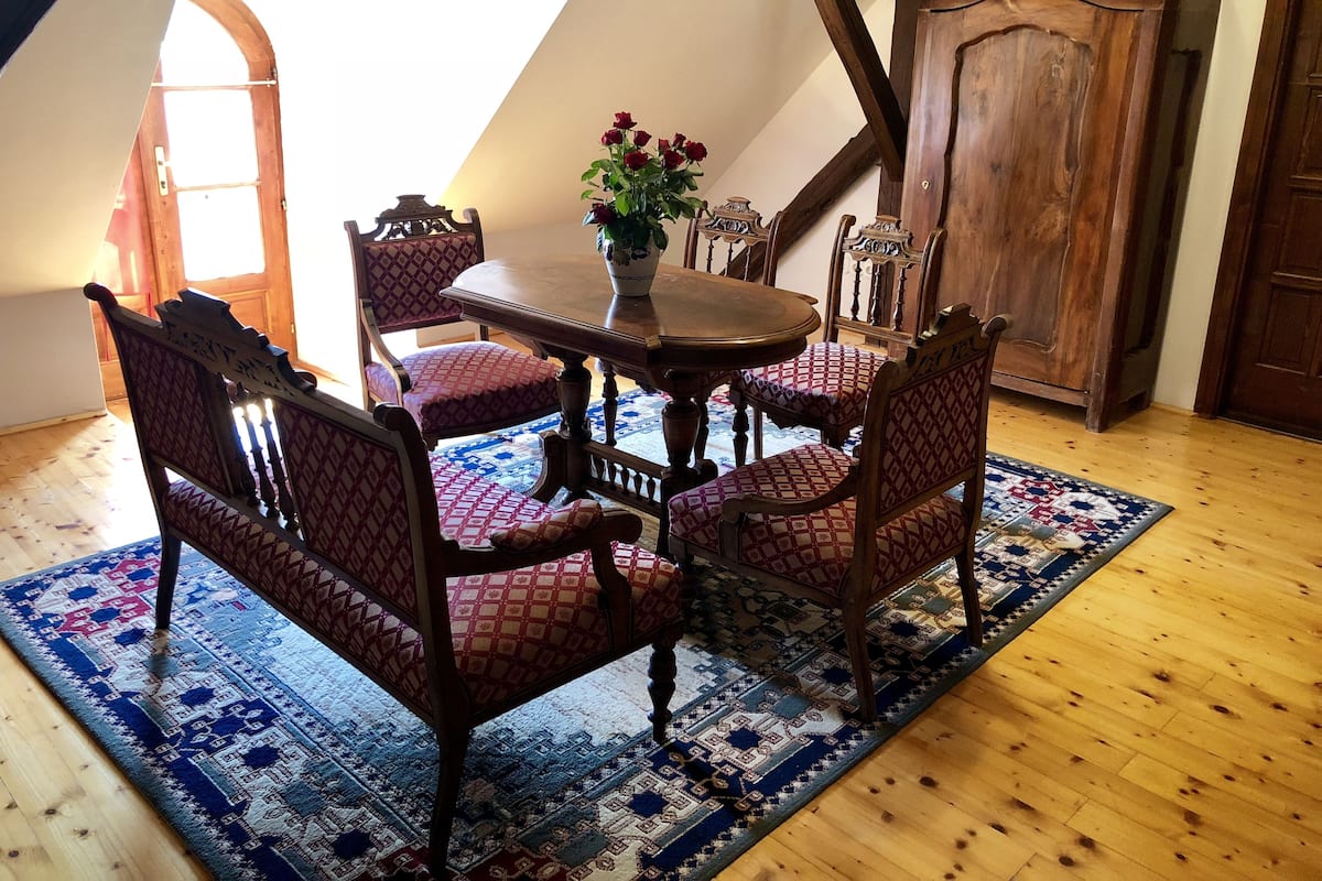 Un coin repas avec une table et des chaises en bois, un tapis à motifs et un vase rempli de fleurs.